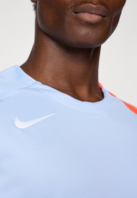 Light blue Nike sports jersey with an orange accent, featuring a white swoosh logo on the front and a textured fabric design.
