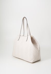 Sac à main beige matelassé avec motif chevrons, design épuré, poignées doubles et couture contrastée. Matériau doux, spacieux, forme structurée.