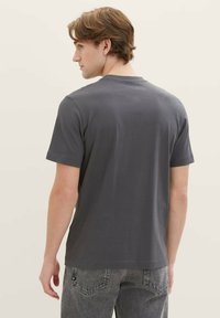 Graues T-Shirt mit kurzen Ärmeln aus weicher Baumwolle, das einen klassischen Rundhalsausschnitt und eine glatte Textur aufweist, kombiniert mit hellgrauen Jeans.