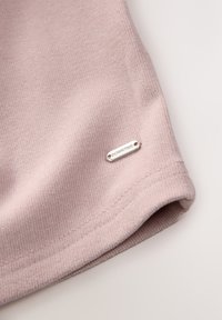 Tessuto per abbigliamento di colore rosa chiaro con una texture a coste, caratterizzato da un'etichetta argentata impressa con la scritta "DOWNTIME" sul bordo inferiore.