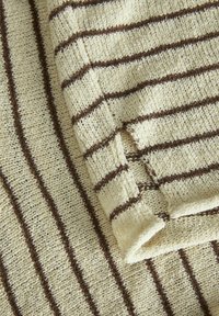 Stickad tyg med en krämfärgad bas och ojämna bruna horisontella ränder, som visar ett texturerat, mjukt material med en fransad kant.