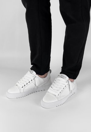 Witte leren sneakers met een gestructureerde afwerking, vetersluiting aan de voorkant, gevoerde kraag en rubberen zool. Gemaakt in combinatie met zwarte broeken.