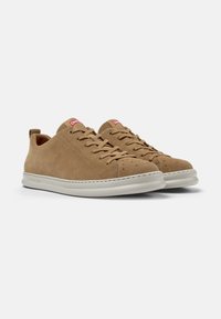 Sneaker basse in suede marrone con suola in gomma bianca, presentano punta rotonda, occhielli e una linguetta sul retro. Logo del marchio rosso sulla linguetta.