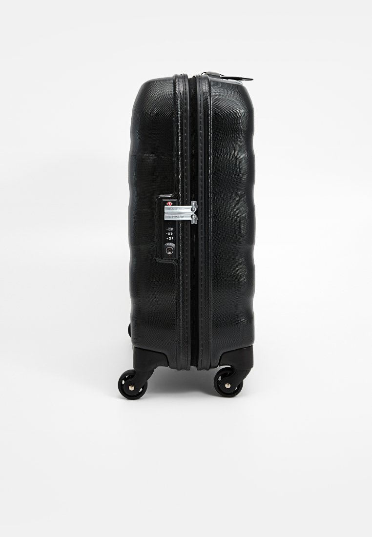 Valise à roulettes noire avec une surface texturée, fermeture à double zip, verrou à combinaison et quatre roulettes lisses. Design compact et robuste.