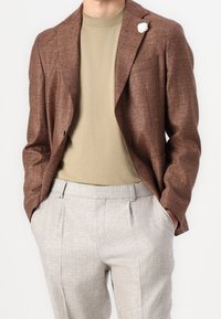 Brun texturerad blazer, beige polo-skjorta och ljusgrå skräddarsydda byxor. Blazern har en vit blommig accent på slaget.