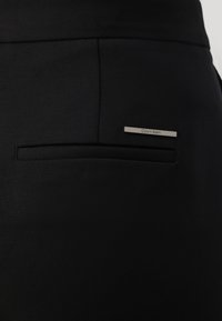 Melna auduma bikses ar elegantu dizainu, ar smalku aizmugures kabatu un sudraba Calvin Klein logotipa akcentu. Gluda tekstūra.