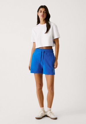Weiße, kurzärmlige, cropped T-Shirt, kombiniert mit hellblauen, knielangen Shorts mit elastischem Bund und seitlichen Taschen.