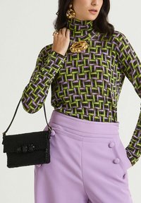 Borsa a tracolla nera con perline, con patta, superficie testurizzata e tre accenti lucidi, abbinata a un dolcevita con motivo verde e viola e pantaloni lilla.