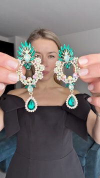 Ašarinės auskarai su žaliais ir violetiniais akmenimis, papuoštais gėlių akcentais. Aukso spalvos detalės ir tekstūruotas paviršius pagerina dizainą.