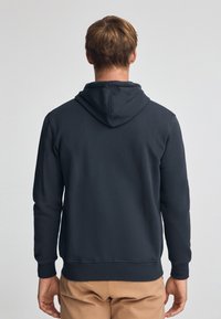 Bluza z kapturem w ciemnoszarym kolorze, wykonana z mieszanki bawełny. Posiada kieszeń kangurzą oraz ściągacze na rękawach. Gładka faktura i luźny krój.