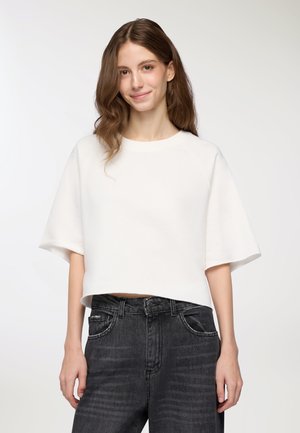 Felpa bianca corta con maniche larghe, texture morbida e scollo rotondo, abbinata a jeans di denim grigio scuro a vita alta.