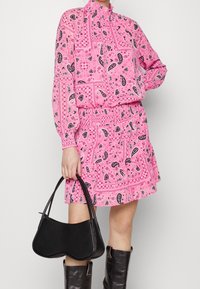 Blouse rose imprimée et jupe avec motifs cachemire, associées à un petit sac à main noir et des bottes noires montantes. Tissu lisse, coupe décontractée.
