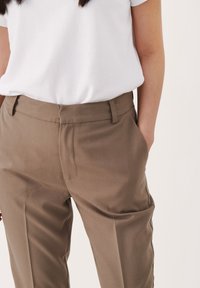 Ljusbruna skräddarsydda byxor med en slät textur, med sidofickor och en ren midja. Matchas med en vit t-shirt.