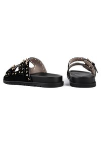 Svarta mockasandaler med guldtonad hårdvara, utrustade med öglor och två parallella remmar. Tjock svart sula, öppen bakdesign.