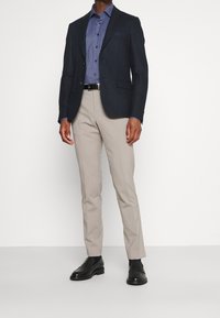 Marinblå kavaj ovanpå en blårutig skjorta, tillsammans med ljusbeiga byxor och svarta finskor. Skräddarsydd passform och mjuka texturer.