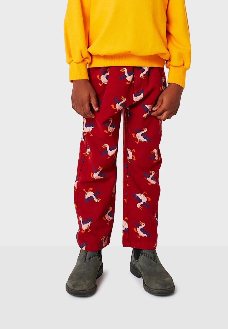 Pantaloni rossi con un divertente motivo di anatra, dotati di una cintura elastica, vestibilità ampia e tessuto testurizzato. Abbinati a un maglione giallo e stivali grigi.