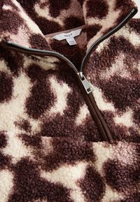 Brun og creme zip-up fleece pullover med kvægprint mønster; har en høj krave, blød tekstur og en sølv lynlås.