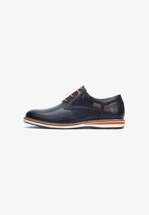 Marineblauw leren schoen met oranje veters, gladde textuur, ronde neus, witte tussenzool en bruine accentstreep. Heeft een gestikte detail.