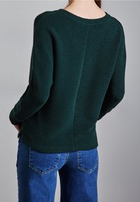 Maglione verde scuro con trama, vestibilità comoda e scollo rotondo, abbinato a jeans blu con design classico delle tasche.