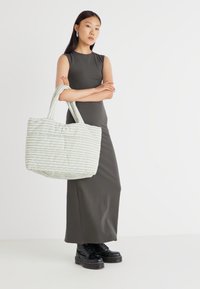 Green and white striped tote bag with intricate texture, spacious design, and sturdy handles, paired with a fitted dark dress and black boots.