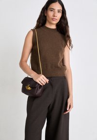Maglione senza maniche marrone, con collo alto, abbinato a pantaloni larghi marrone scuro. Borsa in pelle bordeaux con un'accenno dorato.