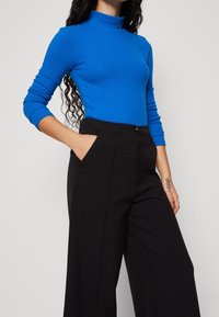 Blå figurpassad polotröja i kombination med högmidjade svarta byxor. Toppen har långa ärmar och en slät textur. Byxorna har sidofickor.