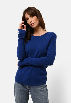 Maglione blu lavorato a maglia con maniche lunghe e colletto rotondo, realizzato in un tessuto morbido. Abbinato a jeans blu chiaro, con una vestibilità comoda.