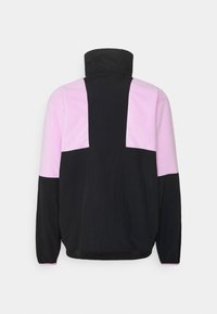 Musta ja vaaleanpunainen fleece-takki, jossa on korkea kaulus ja värierottelu. Takissa on suuret vaaleanpunaiset paneelit harteilla ja yläselässä.