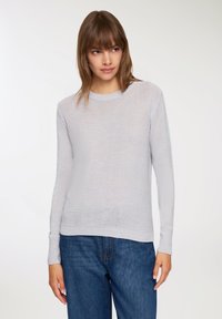 Maglione grigio chiaro lavorato a maglia con maniche lunghe, colletto rotondo, polsini e orlo a coste. Taglio rilassato con una texture leggera. Abbinato a jeans in denim blu.
