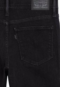 Poche arrière d'un jean en denim noir avec un patch en cuir marqué Levi’s et une petite étiquette en tissu Levi’s sur la couture latérale.