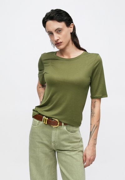 Tricou cu mâneci scurte de culoare verde măsliniu, realizat dintr-un material fin, asortat cu pantaloni verde deschis și o curea maro cu o cataramă aurie.