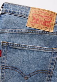 Jeans de mezclilla azul claro con una etiqueta de cuero que muestra "Levi Strauss & Co." y detalles de diseño como bolsillos cosidos y un patrón de costura distintivo.