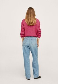 Pull en tricot rose à coupe décontractée, associé à un jean taille haute bleu clair. La texture est côtelée, avec des coutures et des poches visibles.