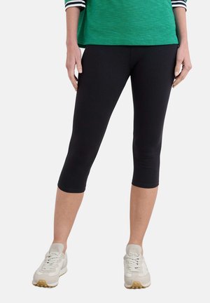 Sorte, knælange leggings lavet af strækbart stof, med en glat overflade og en tætsiddende design, parret med lyse sportsko.