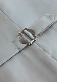 Close-up of silver metal buckle fastening a folded light grey fabric strap on matching fabric background.