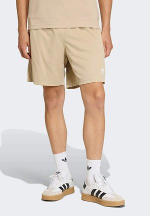 Beżowe sportowe szorty o teksturowanym, siateczkowym wzorze, z białym logo, w połączeniu z białymi i czarnymi butami sportowymi oraz białymi skarpetkami z logo.