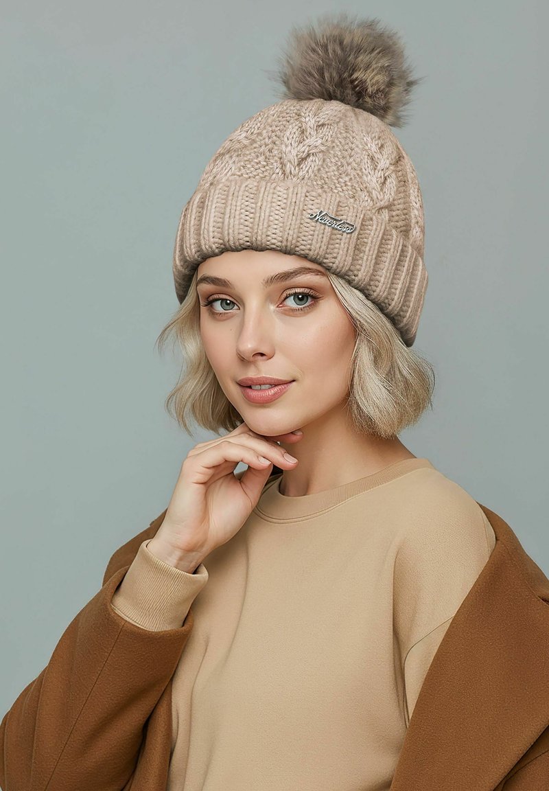 Knit beige beanie with a textured pattern and a fluffy pom-pom on top. Features a small silver logo on the front.