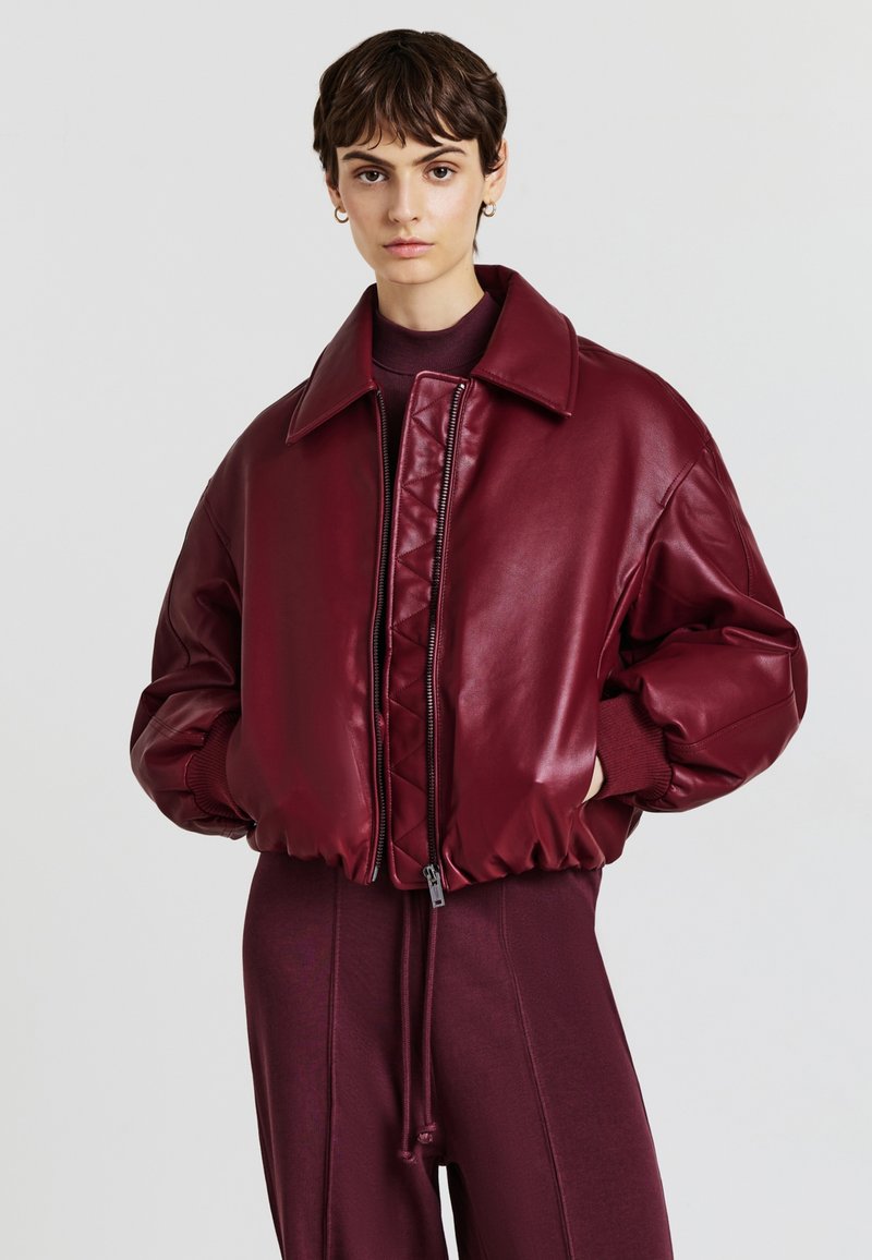 Giacca bomber in eco-pelle bordeaux con parte frontale trapuntata, taglio oversize, collo a pressione e polsini a costine. Abbinata a pantaloni coordinati.