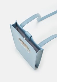 Jasnoniebieska skórzana torba na ramię z nadrukiem dwóch anielskich twarzy i białym napisem na przedniej klapie, na białym tle.