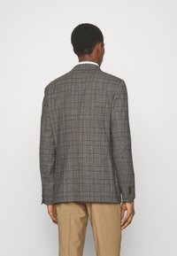Grau kariertes Blazer aus strukturiertem Stoff. Verfügt über einen zwei-Knopf-Verschluss, Reverskragen und taillierte Passform. Getragen über beigen Hosen.