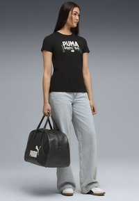 Sort bomulds T-shirt med hvid "PUMA" logo, parret med lyseblå denim jeans og en sort læder duffel taske med et hvidt logo.