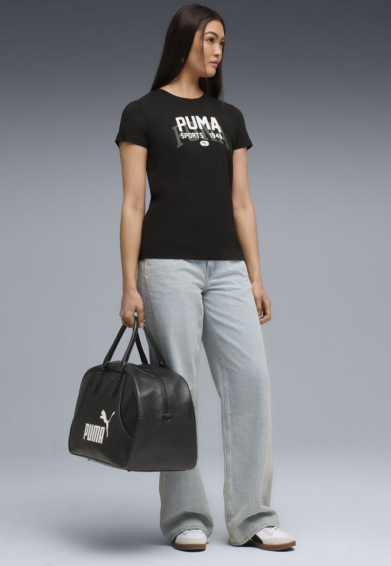 Sort bomulds T-shirt med hvid "PUMA" logo, parret med lyseblå denim jeans og en sort læder duffel taske med et hvidt logo.