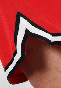 Červené sportovní tričko s texturovaným vzorem a černobílým proužkovaným lemem podél okrajů.