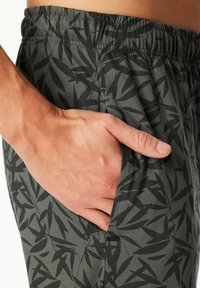 Hand resting inside the side pocket of gray elastic-waist shorts with a black abstract leaf pattern.
