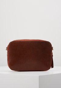 Borsa a tracolla in pelle marrone di forma rettangolare, con texture liscia, bordi arrotondati e un piccolo dettaglio con nappina laterale.
