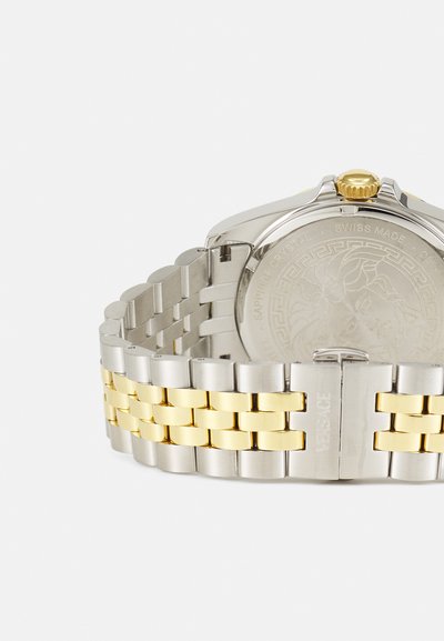 Montre en argent et or avec un bracelet en métal, dotée d'un boîtier rond, d'une couronne texturée et d'un fond gravé avec un design de lion.