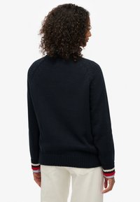 Pull en maille bleu marine avec poignets côtelés ornés de rayures rouges, blanches et bleues. Coupe décontractée et tissu texturé avec un col haut.