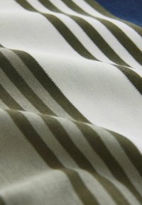 Tissu blanc à rayures horizontales vert olive et vert foncé, présenté en gros plan avec une texture visible et des plis doux.