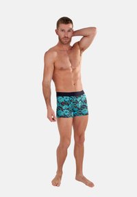 Men’s trunks featuring a floral pattern in turquoise and black, made from stretch fabric with a dark elastic waistband.