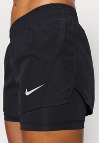 Mustat urheilushortsit, jotka on valmistettu kevyestä kankaasta. Niissä on hengittävä verkkopaneeli, joustava vyötärö ja valkoinen Nike-logo sivulla.